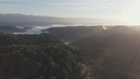 Luftaufnahme-Eines-Sees-Inmitten-Von-Bergen-Bei-Sonnenuntergang,-Mit-Etwas-Nebel-über-Dem-See-Zwischen-Den-Grünen-Bergen-In-Kolumbien