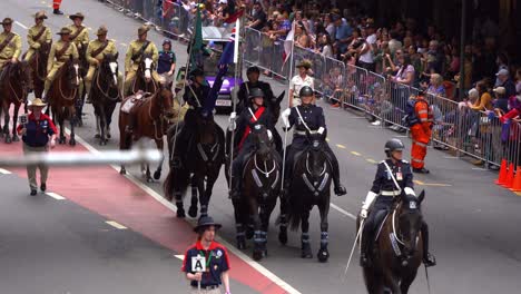 Unidad-Montada-Del-Servicio-De-Policía-De-Queensland-Cabalgando-Por-La-Calle-Durante-El-Desfile-Del-Día-De-Anzac,-Aplaudiendo-A-La-Multitud-A-Lo-Largo-De-La-Calle-Con-Multitudes-Aclamando-A-Lo-Largo-De-La-Calle