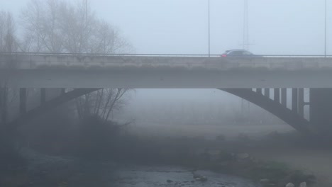 Coches-Pasando-Por-Un-Puente-Misterioso-Con-Mucha-Niebla-Y-Un-Río-Debajo.