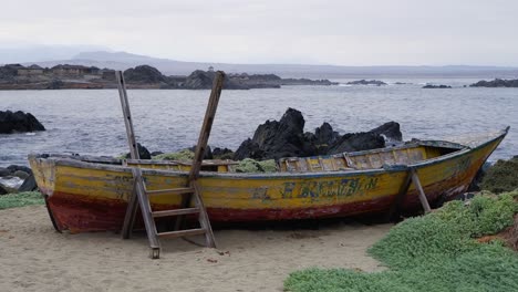 Rustic-old-wooden-fishing-boat-propped-up-on-rugged-rocky-ocean-shore