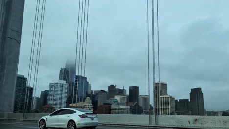 Driving-POV-crossing-San-Francisco-bridge,-USA-tall-buildings-Tesla-Volvo-cars