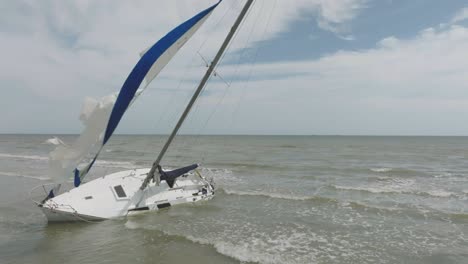 An-aerial-drone-view-of-a-sailboat-run-aground-on-Galveston-beach-on-Galveston-Island,-Texas