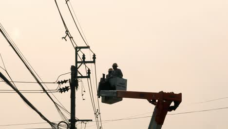 Two-electricians-wearing-hard-hats,-in-a-railed-aerial-platform,-attached-to-a-hydraulic-crane-or-a-boom-lift,-are-being-lowered,-Bangkok,-Thailand