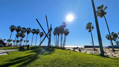 Panorama-Tageslicht-Am-Venice-Beach-In-Los-Angeles,-Kalifornien,-Stadtpark-Mit-Weißem-Sand,-Leute-Fahren-Mit-Dem-Fahrrad-Auf-Der-Küstenstraße,-Zeitlupen-Schwenkaufnahme-Der-Skyline-Bei-Sonnenschein