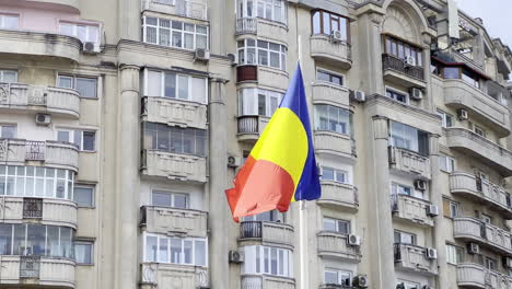 Bandera-Nacional-De-Rumania-En-Un-Día-Ventoso-Con-Bloques-Comunistas-Desgastados-Y-Grises-Para-La-Clase-Media,-Como-Fondo