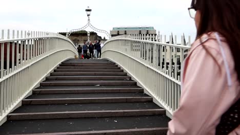 Back-view-of-woman-walking-the-steps-of-Ha'penny-Bridge-in-Liffey-River,-Dublin