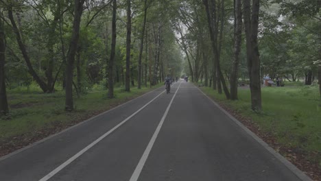 4k-50fsp,-Frau-Fährt-Fahrrad-Auf-Einer-Straße,-Die-In-Einen-Wald-Führt,-Ein-Privater-Fahrradweg,-Umgeben-Von-Dichten-Grünen-Bäumen,-Sommer