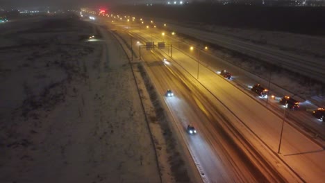 A-snowy-highway-in-montreal-at-dusk-with-traffic-lights-blurring-by,-aerial-view