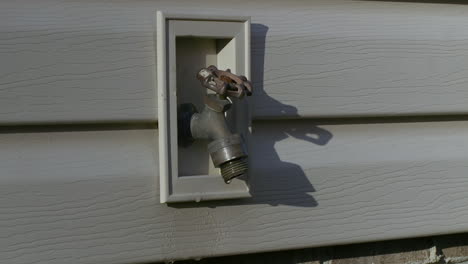 Freshwater-spigot-on-side-of-house,-with-water-dripping-out-slowly
