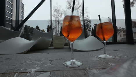 Couple-hands-grabbing-Two-cups-of-soft-orange-drinks-at-hotel-resort-closeup,-cold-beverage-with-straw,-hotel-living-room