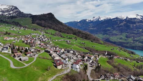 Aerial-view-showing-swiss-village-on-green-hill-with-Lake-Walen-in-the-valley