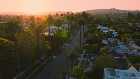 Drone-Over-Beverly-Hills-at-Sunset,-Birds-Eye-View-of-Golden-Hour-on-Iconic-Historic-Street-with-Palm-Trees-and-Luxury-Estates