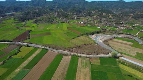 El-Río-Fluye-A-Través-De-Parcelas-Verdes-En-Un-Paisaje-De-Aldea:-Tierras-Cultivadas-Que-Prosperan-En-Primavera,-Enclavadas-En-Un-Hermoso-Valle-En-Albania