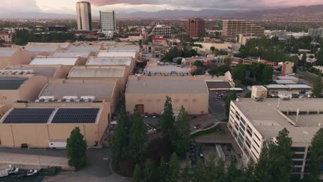 Drone-Flying-Over-WB-Lot-at-Daytime,-Aerial-Shot-Moving-Right-to-Left-Over-Sound-Stages-with-Grip-Trucks-Parked-in-Formation