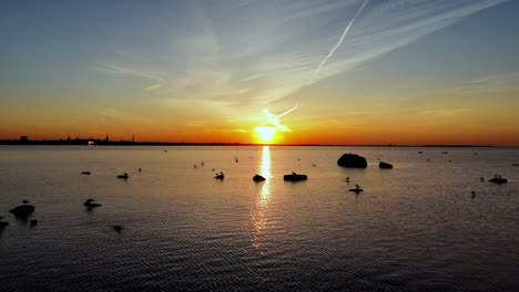 Sunrise-skyline-drone-fly-above-ocean-waters-gradient-sky-skyline-shining,-rocks-float-in-calm-still-water,-aerial-view