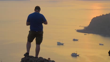 Man-Standing-On-The-Summit-With-Boats-Floating-In-The-Sea-During-Golden-Hour-In-Padar-Island,-Indonesia