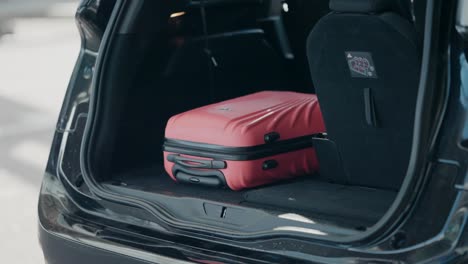 Coral-suitcase-in-open-car-trunk-at-the-airport