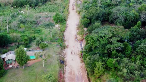 Aéreo-Siguiendo-Un-Camino-Que-Pasa-Sobre-El-Bosque-De-Paraguay-Con-Niños-Caminando-Cuesta-Arriba-De-Regreso-A-Sus-Casas.