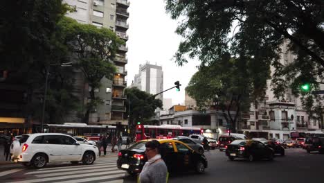 Geschäftiger-Stadtverkehr-Auf-Der-Alberdi-Avenue-In-Buenos-Aires,-Fußgänger-Auf-Einer-Asphaltierten-Straße-Mit-Bäumen