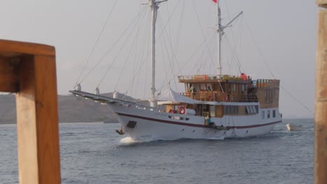 Barco-Turístico-Navega-Por-El-Mar-Visto-Desde-Otro-Yate-Con-La-Isla-De-Komodo-Al-Fondo