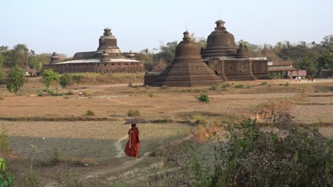 Un-Monje-Budista-Camina-Frente-Al-Shite-thaung-tempel-Y-Al-Templo-Htukkant-Thein,-Mark-U,-Estado-De-Rakhine,-Myanmar