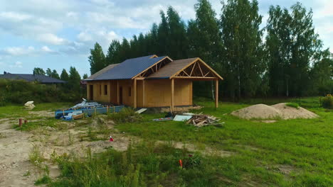 Aerial-drone-fly-above-wooden-house-with-solar-panels-under-construction-forest-countryside-location-with-sunny-skyline