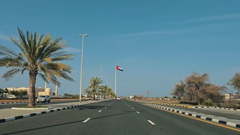 A-car-drives-towards-the-UAE-flagpole-on-a-clear-day-in-the-eastern-region-of-the-United-Arab-Emirates