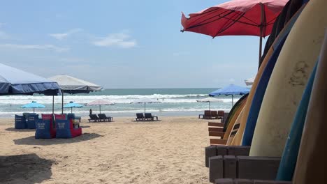 Tablas-De-Surf-Y-Sombrillas-En-La-Playa-De-Legian-En-Bali,-Indonesia,-Soplando-Con-La-Brisa.