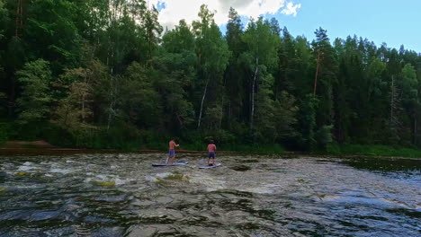 People-board-paddling-on-wavy-river-water-in-Gauja-national-park,-view-from-kayak