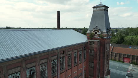 Backward-Aerial-Moving-Away-From-Old-Factory-Building-With-Tower-Feature