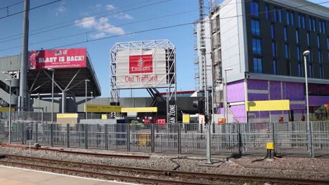 Yellow-tram-passes-by-Old-Trafford-stadium-in-Manchester-on-sunny-day,-passengers-visible