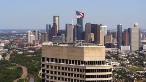 Toma-De-Establecimiento-De-Una-Bandera-Estadounidense-Ondeando-En-El-Viento-En-Lo-Alto-De-Un-Rascacielos-En-Houston