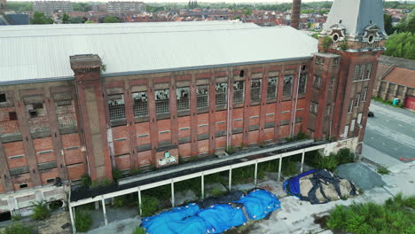 Downward-Dolly-Aerial-of-Old-Abandoned-Building-With-Blue-Construction-Tarps-in-Ghent
