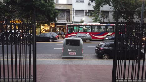 Errichtung-Des-Eingangszauns-Zur-Latin-American-Avenue.-Frau-Läuft-Am-Auto-Vorbei,-Verkehr-Bei-Sonnenuntergang-Im-Süden,-Rivadavia-Avenue