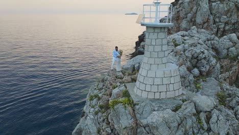 Kalamota-Island,-Adriatic-Sea,-Croatia---A-Couple-Basking-in-the-Sunset's-Glow-by-the-Lighthouse---Pan-Up-Shot