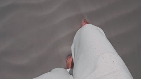 A-person-in-white-sweat-pants-walking-barefoot-over-a-white-sandy-beach