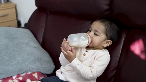 Un-Niño-De-18-Meses-Bebiendo-Leche-De-Un-Biberón-Sentado-En-Un-Sofá,-Capturando-Un-Concepto-Atemporal-De-Crianza-Y-Nutrición