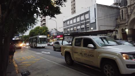 Rivadavia-avenue-traffic-at-latin-city-urban-sunset-church-school-pedestrians-walk-by-Lourdes-church-catholic-town