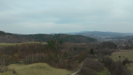 Aerial-backwards-shot-of-hilly-forest-landscape-during-cloudy-day-in-Poland