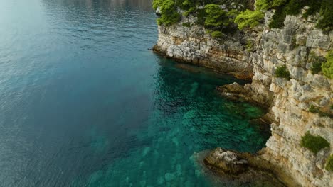 Isla-De-Kalamota,-Mar-Adriático,-Croacia---Las-Serenas-Y-Cristalinas-Aguas-Azules-Se-Encuentran-Con-La-Escarpada-Costa---Drones-Volando-Hacia-Adelante