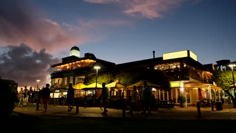 Besucher-Gehen-Vor-Beleuchteten-Restaurants-Der-Hermanus-Waterfront,-Dämmerung