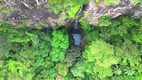Descending-over-the-Oque-Pipi-waterfall,-with-the-water-falling-creating-a-lake-on-Príncipe-Island,-in-São-Tomé,-Africa