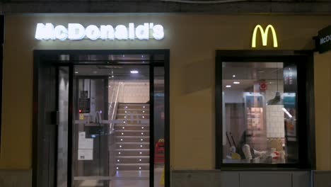 Por-La-Noche,-Una-Niña-Cena-Dentro-De-Un-McDonald&#39;s,-Una-Cadena-De-Comida-Rápida-Estadounidense,-Mientras-Un-Peatón-Pasa