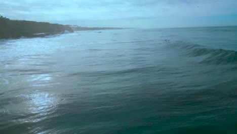 Drone-Shot-of-two-pelicans-flying-with-the-waves-on-the-Carlsbad-Coastline-on-a-cloudy-day