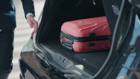 Man-unloading-bright-pink-suitcase-from-car-trunk