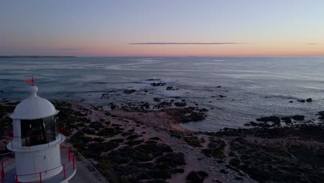 Corny-Point-lighthouse-aerial-reveal-shot-with-flashing-light-beacon-at-dusk,-Yorke-Peninsula,-South-Australia