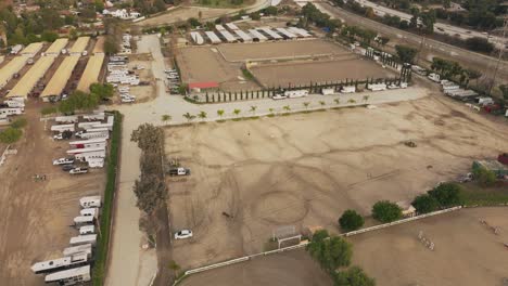 Aerial-Shot-of-LA-Equestrian-Center-in-Daytime,-Drone-Approaching-Horse-Running-in-Circular-Pattern-in-Training-Pen