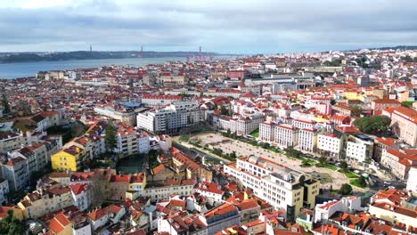 Flying-backwards-over-the-city-of-Lisbon,-with-view-from-Martim-Moniz-square,-with-Lisbon-cityscape-and-tejo-river-in-the-background,Portugal