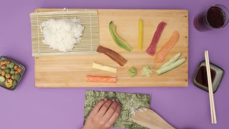 Top-shot-of-two-Hands-preparing-Sushi-on-violet-table