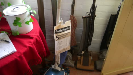 Vintage-hoover-vacuum-cleaners-in-a-rustic-room,-with-tile-floors-and-a-red-tablecloth,-evoke-a-sense-of-past-domestic-life